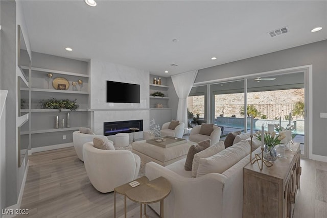 living room featuring a healthy amount of sunlight, light wood finished floors, visible vents, and a high end fireplace