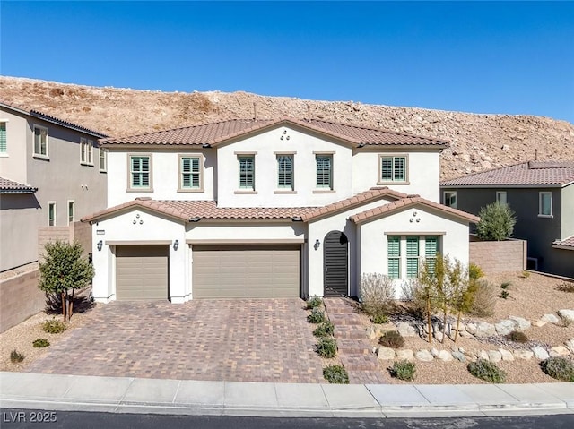 mediterranean / spanish-style home with a garage, decorative driveway, a mountain view, and stucco siding