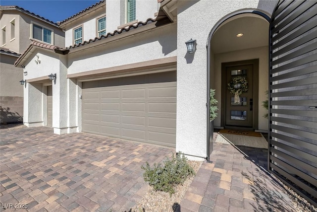 entrance to property with a garage, decorative driveway, a tile roof, and stucco siding