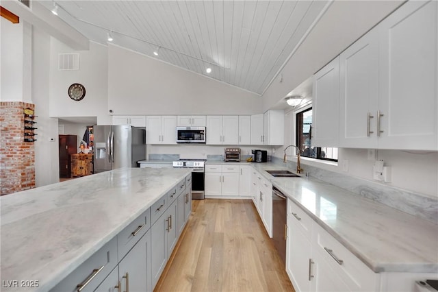 kitchen with appliances with stainless steel finishes, light wood-style floors, white cabinets, a sink, and light stone countertops