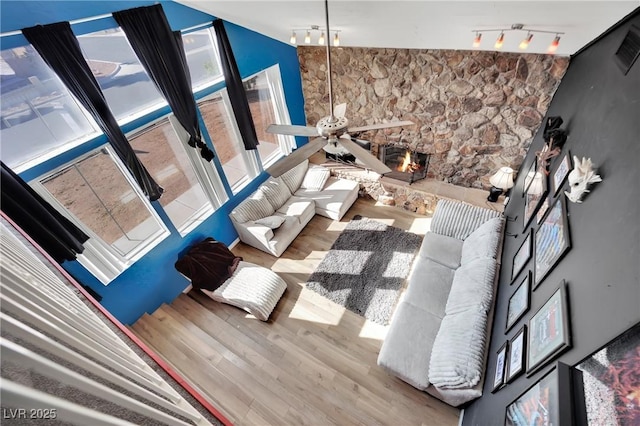 unfurnished living room with ceiling fan, a stone fireplace, wood finished floors, and rail lighting