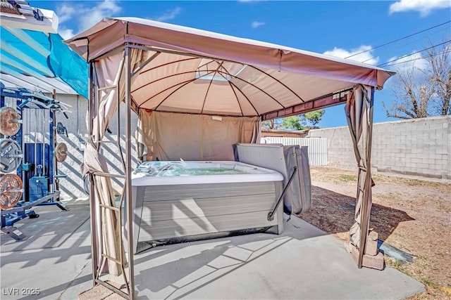 view of patio / terrace featuring a hot tub, a fenced backyard, and a gazebo