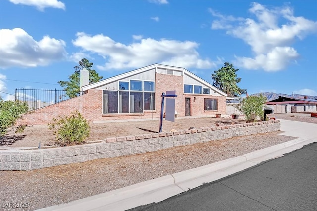 mid-century modern home with concrete driveway, brick siding, a chimney, and fence