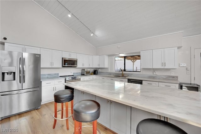 kitchen with light stone counters, a sink, white cabinetry, a kitchen breakfast bar, and appliances with stainless steel finishes