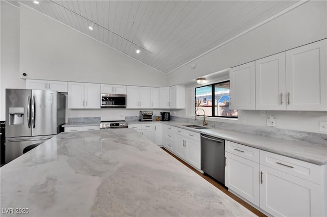 kitchen featuring light stone countertops, appliances with stainless steel finishes, white cabinets, and a sink