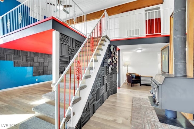 stairway with a towering ceiling, a wood stove, baseboards, and wood finished floors