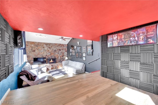 interior space featuring a ceiling fan, vaulted ceiling, a stone fireplace, and wood finished floors