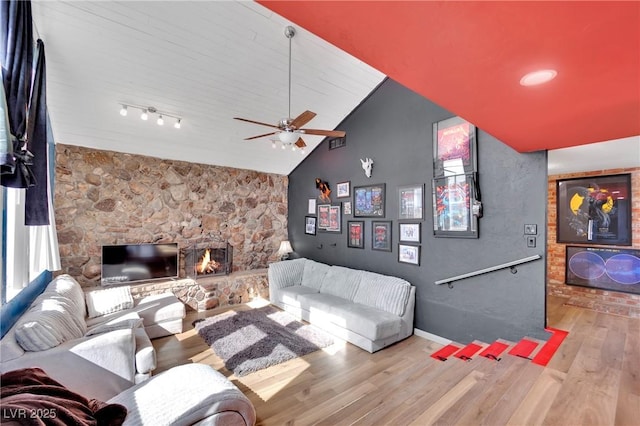 living area with baseboards, ceiling fan, wood finished floors, a stone fireplace, and high vaulted ceiling