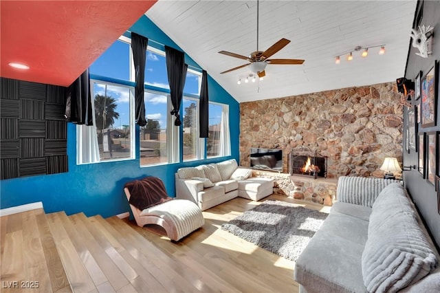 living room with lofted ceiling, a stone fireplace, wood finished floors, and rail lighting