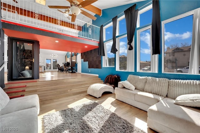 living room with ceiling fan with notable chandelier, a high ceiling, and wood finished floors