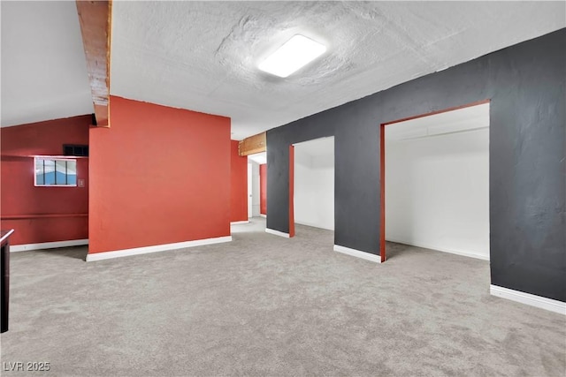 interior space featuring lofted ceiling, carpet, baseboards, and a textured ceiling