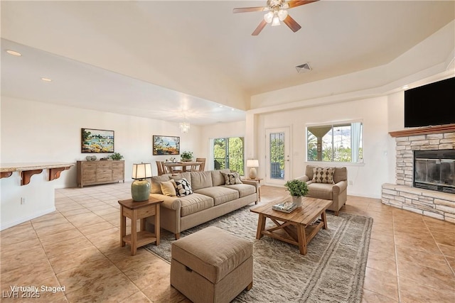 living room featuring a stone fireplace, ceiling fan, and light tile patterned flooring