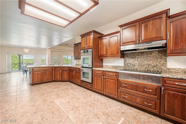 kitchen with tasteful backsplash, light stone counters, kitchen peninsula, stainless steel double oven, and black electric cooktop