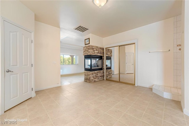 unfurnished bedroom with a stone fireplace, light tile patterned floors, and a closet