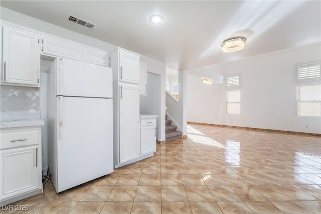 kitchen featuring white refrigerator, light tile patterned floors, white cabinets, and backsplash