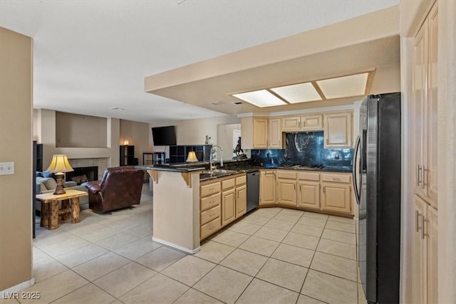 kitchen with light tile patterned floors, a tile fireplace, black refrigerator, stainless steel dishwasher, and kitchen peninsula