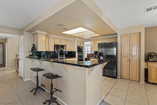 kitchen with dark stone countertops, kitchen peninsula, light tile patterned floors, and black appliances