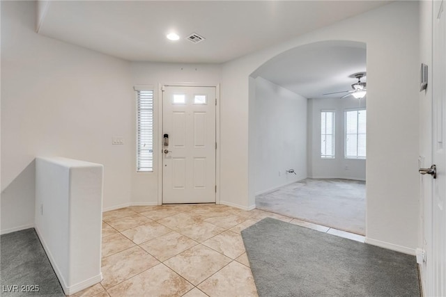 entrance foyer featuring light tile patterned floors, a ceiling fan, visible vents, baseboards, and arched walkways