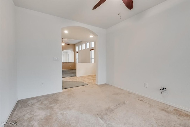 empty room with arched walkways, baseboards, a ceiling fan, and carpet floors