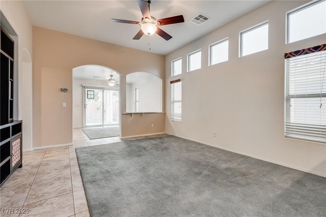 unfurnished living room with light tile patterned floors, baseboards, visible vents, arched walkways, and ceiling fan