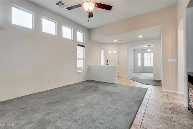 empty room featuring visible vents, a ceiling fan, arched walkways, light tile patterned floors, and baseboards