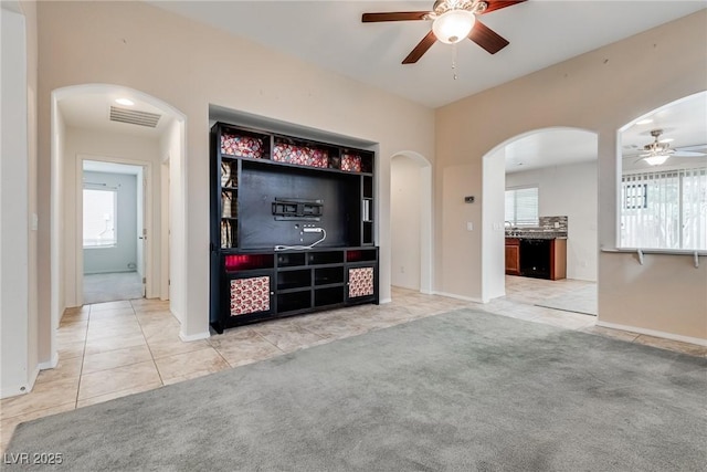 unfurnished living room featuring tile patterned floors, visible vents, a ceiling fan, arched walkways, and carpet flooring