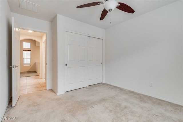 unfurnished bedroom with visible vents, baseboards, a closet, light carpet, and arched walkways