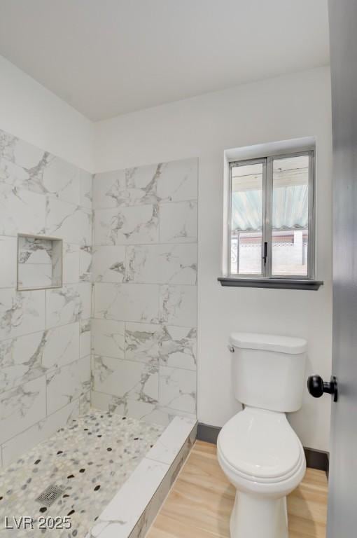 bathroom with tiled shower, toilet, and hardwood / wood-style floors