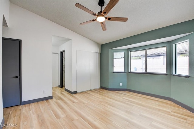 spare room with a textured ceiling, vaulted ceiling, ceiling fan, and light wood-type flooring