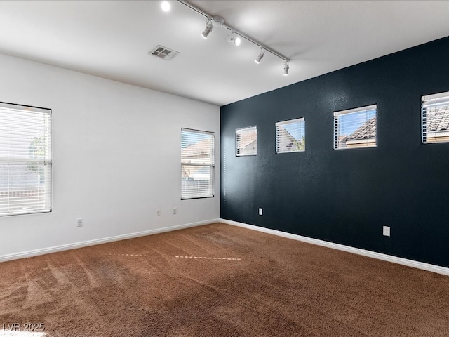 empty room with carpet, rail lighting, visible vents, and baseboards