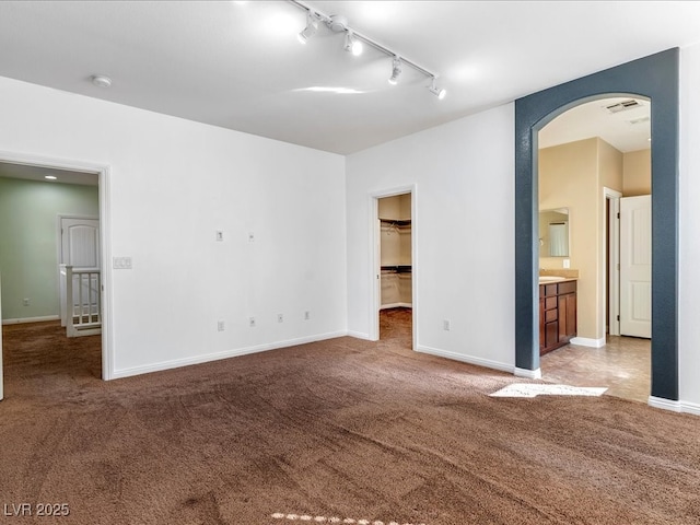 carpeted spare room featuring track lighting, arched walkways, visible vents, and baseboards