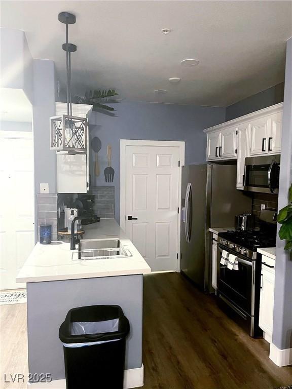 kitchen with a sink, dark wood-style floors, stainless steel appliances, a peninsula, and decorative backsplash