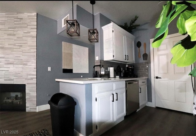 kitchen featuring dark wood finished floors, dishwasher, light countertops, a fireplace, and white cabinetry