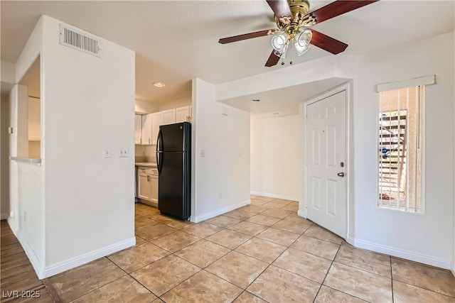 kitchen with black refrigerator, white cabinetry, plenty of natural light, and light tile patterned flooring