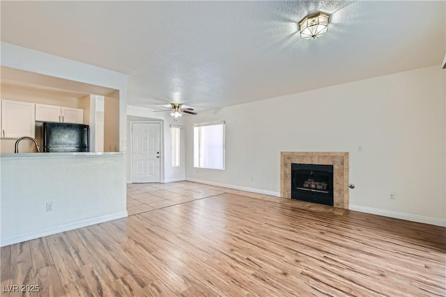 unfurnished living room with ceiling fan, a textured ceiling, a fireplace, and light wood-type flooring