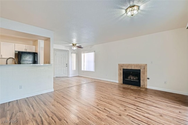 unfurnished living room featuring a tiled fireplace, ceiling fan, a textured ceiling, and light wood-type flooring