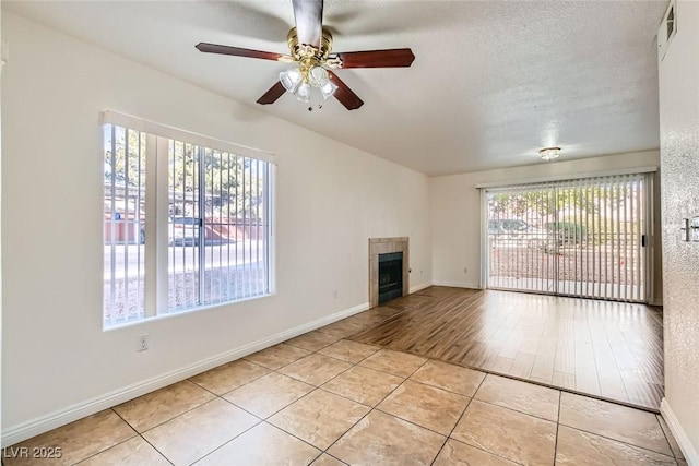 unfurnished living room with light tile patterned flooring, ceiling fan, a tile fireplace, and a textured ceiling