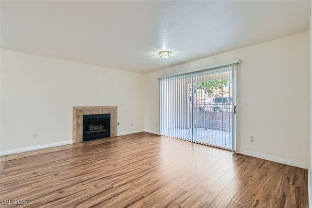 unfurnished living room with a tiled fireplace, a textured ceiling, and light wood-type flooring