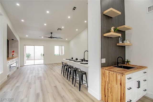 kitchen with visible vents, a sink, light wood-style flooring, wood counters, and open shelves