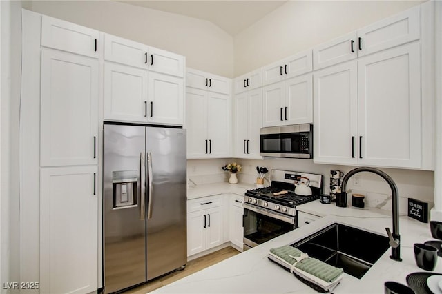 kitchen with light stone countertops, lofted ceiling, appliances with stainless steel finishes, white cabinets, and a sink