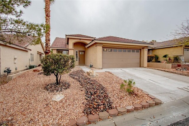 mediterranean / spanish-style house with central air condition unit, a tile roof, stucco siding, driveway, and an attached garage