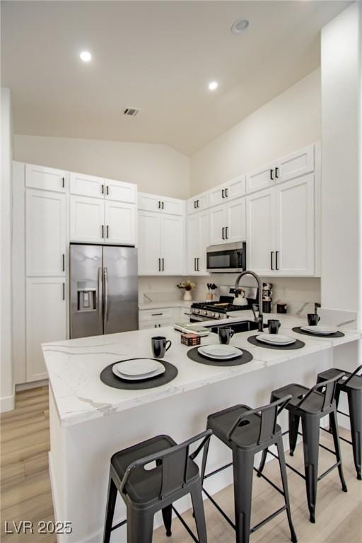 kitchen with visible vents, a breakfast bar, lofted ceiling, appliances with stainless steel finishes, and white cabinetry