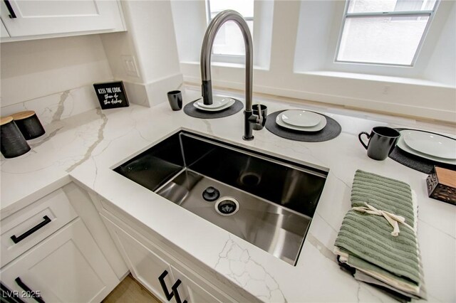 details featuring white cabinetry, light stone counters, and a sink