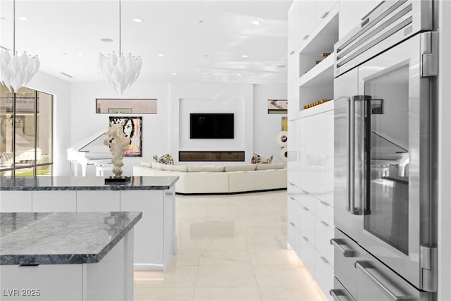 kitchen with recessed lighting, high end refrigerator, white cabinetry, dark stone countertops, and decorative light fixtures