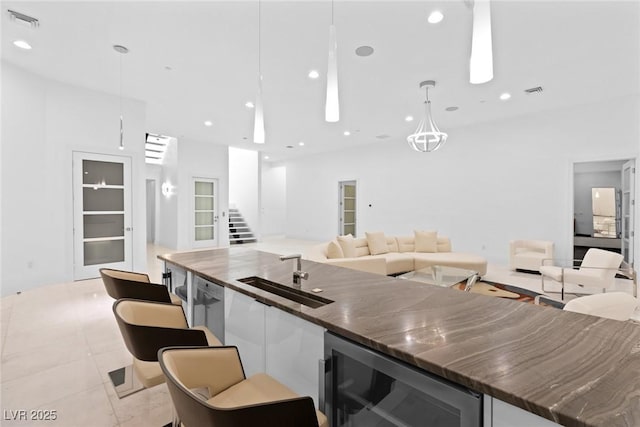 kitchen with wine cooler, pendant lighting, dark countertops, open floor plan, and a sink