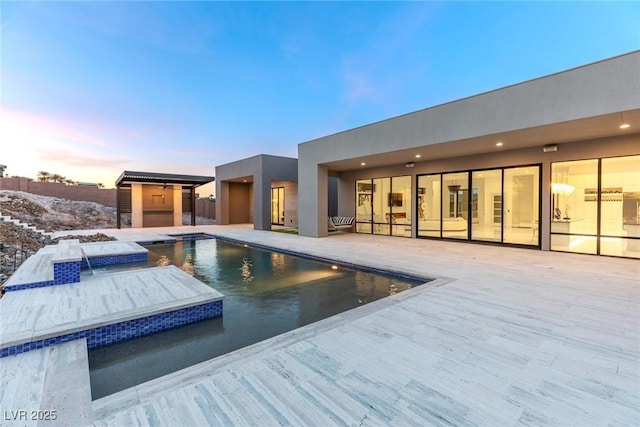 pool at dusk with a jacuzzi, an outdoor pool, a patio, and an outdoor structure