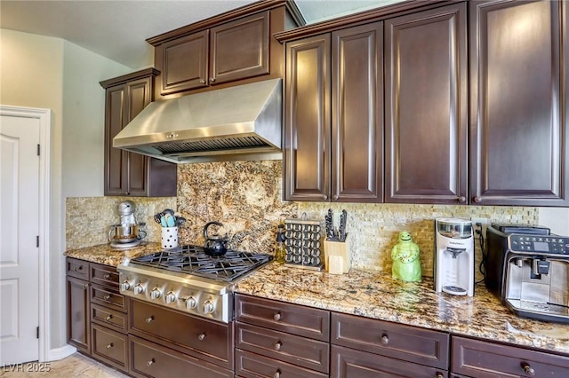 kitchen with light stone counters, wall chimney range hood, tasteful backsplash, and stainless steel gas stovetop