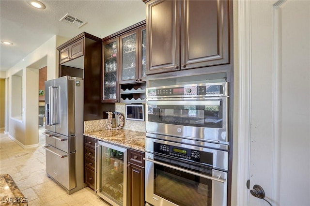 kitchen with light stone counters, dark brown cabinets, stainless steel appliances, and beverage cooler