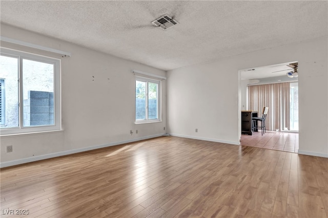 spare room with baseboards, visible vents, a textured ceiling, and light wood finished floors