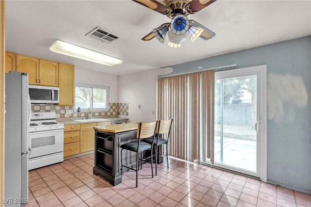 kitchen featuring stainless steel microwave, visible vents, light brown cabinetry, freestanding refrigerator, and white gas range oven